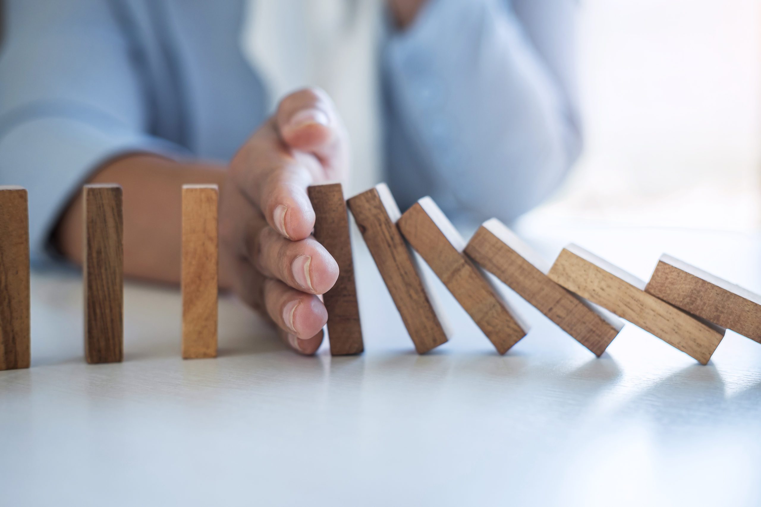 Risk and Strategy in Business, Image of hand stopping falling collapse wooden block dominoes effect from continuous toppled block, prevention and development to stability